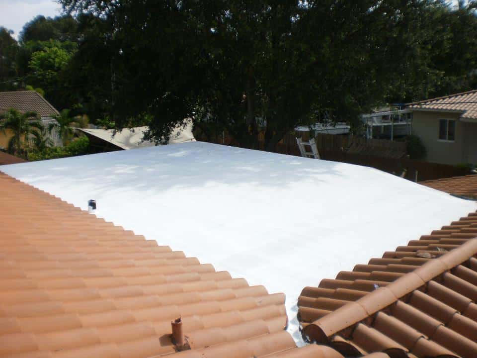Worker applying protective roof coating on a flat roof in South Florida