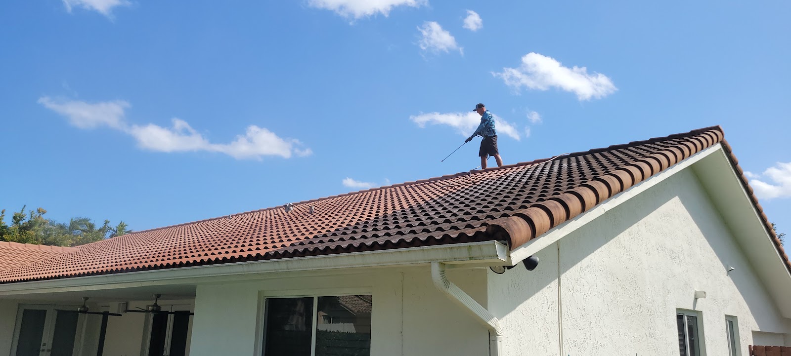 Roof cleaning technician soft-washing black algae streaks off a Miami tile roof